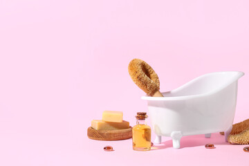 Small bathtub, massage brush, soap and essential oil on pink background