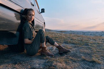 Woman sitting next to car in the middle of field enjoying a peaceful travel moment