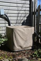 An outdoor central air conditioning condenser unit is covered with a protective beige storage cover...