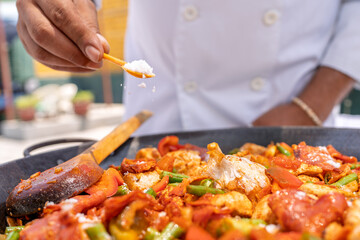 Chef adding salt to paella with chicken and vegetables