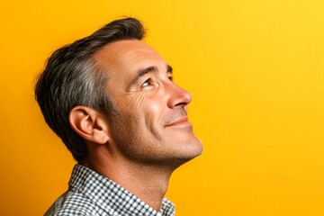 Fototapeta premium Idea of style for aging men. Elegant men's wavy bob haircut - midlife white man with black hair. A peaceful and elegant male enjoying his moment. Yellow solid background.