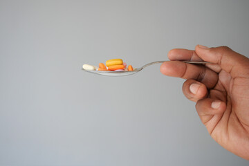 Hand holding a spoon with various colorful pills in plain setting