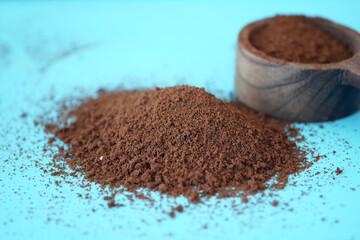 Ground coffee placed next to a wooden scoop on a blue surface