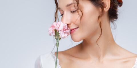 A serene portrait of a woman gently sniffing a soft pink flower with her eyes closed. The clean,...