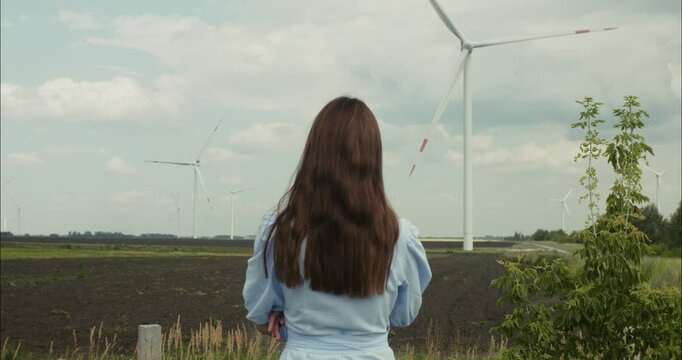 Young woman observing rotating wind turbines in a field