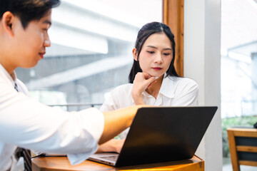 Fototapeta premium Focused discussion: Man explains to woman at a laptop in a bright modern professional space