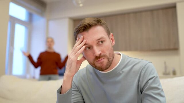 Frustrated exhausted man rolls eyes tired of constant fights, woman in background yelling waving hands. Accusations infidelity, marriage conflict, love faded, emotional strain, relationship fall apart