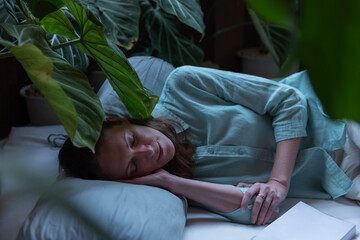 A woman peacefully sleeps on a pillow surrounded by lush green plants, creating a serene and natural environment. Her relaxed posture and calm expression reflect deep rest and connection to nature.