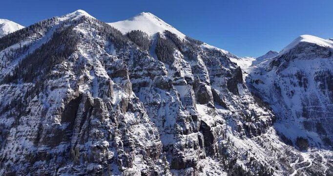 An unworldly aerial drone shot of the extreme Kroger Via Ferrata cliff face and the Black Bear pass switchbacks and summit, slowly tracking forward over the Telluride Valley floor in Western Colorado.