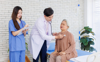 Fototapeta premium Asian senior woman sit on bed while consulting with doctor and caring nurse checking in hospital, Healthcare elderly patient and medical professional support muscle injury consultation wellness being.