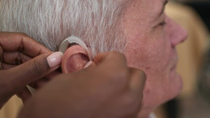 Closeup of unrecognizable hands of caregiver gently adjusting hearing aid on elderly man ear