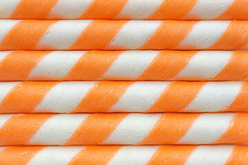Striped wafer rolls filled with orange on white background. Top view