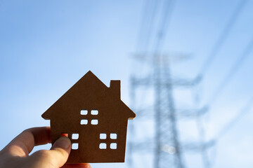 Wooden house signs with large electric pole in the background, concept of electricity bills, rising consumption costs and increasing electricity usage.