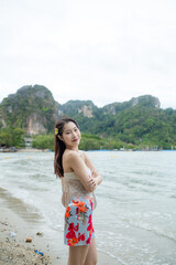 A woman is standing on a beach with a floral dress and a flower in her hair