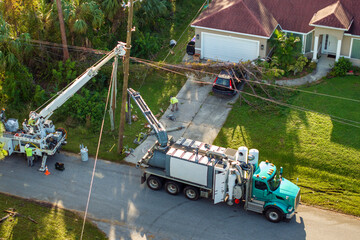 Utility services fixing damaged power lines after hurricane in Florida. Workers using bucket trucks to repair blown down electrical wires at residential home