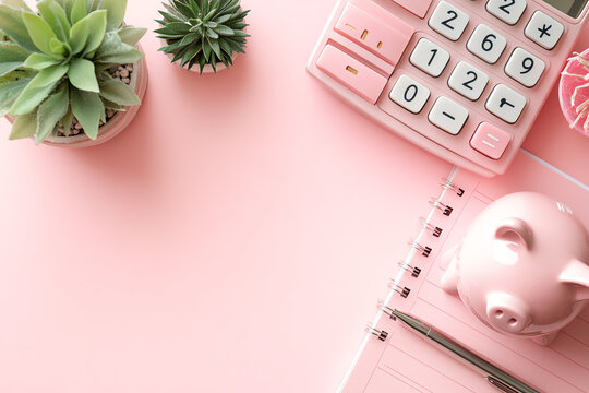 A flat lay of a pink calculator, piggy bank, notebook, pen, and succulents on a pink background.  Perfect for financial planning and budgeting content.