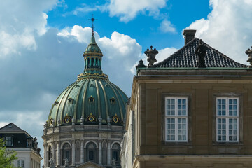 Magnificent copper dome of Frederik's Church (Marble Church) contrasts with adjacent classical Amalienborg Palace facade showcasing impressive Rococo architecture. Partly cloudy blue sky in Copenhagen