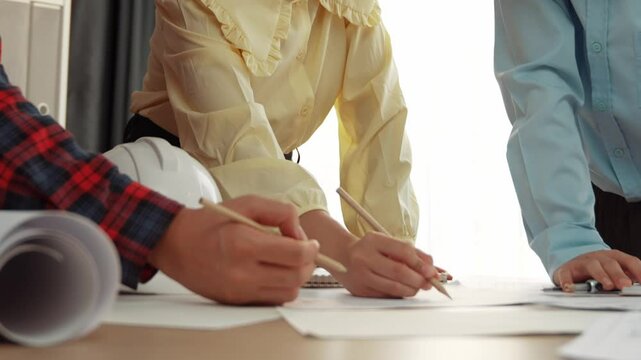 Smart architect and safety engineer discussion about building blueprint on table with architectural document, measurement tools and wooden block scatter around at modern office. Closeup. Delineation.