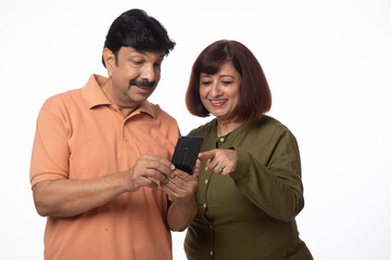 Indian happy senior couple using digital mobile technology on white background. Mobile banking anywhere 