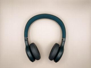 Full-size large headphones made of green plastic with soft earphones and a soft headband lie in the center of the image on a beige background one item