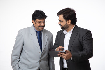 Indian successful businessman using digital tech tablet while standing inside office. Two businessmen watching tablet feeling happy for trade stock, Business growth concept, marketing strategy 