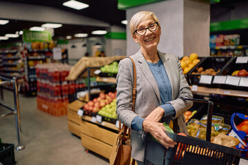 Happy senior woman with shopping basket at supermarket looking at camera.