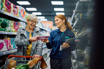 Happy supermarket worker assisting senior woman with shopping at store.