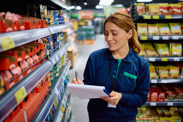 Smiling female worker taking inventory while working at supermarket.