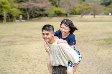 Fototapeta premium Spring scene in May at a no-people park in Jokojicho, Seto City, Aichi Prefecture. A Japanese couple in their early 20s spending time together. He's carrying her on his back.