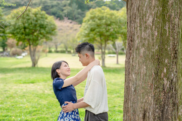 Fototapeta premium In the spring scene in May, we see an unmanned park in Jokojicho, Gokojicho, Eri Prefecture. Japanese couples in their early 20s spend time together.They stare at each other by a large tree.