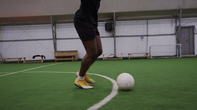 A dolly tracking shot follows a Black football player in a pink bandana and black uniform running with a soccer ball across the field.