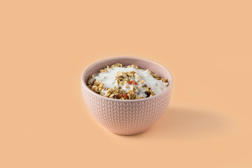 Granola with yogurt . Side view of a ceramic bowl with granola  and yoghurt on the light orange background . Muesli with dried fruit close-up . 
