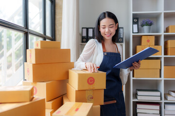 Young asian entrepreneur managing retail orders and preparing packages for dispatch from her warehouse, smiling while checking inventory and ensuring smooth logistics for her online business