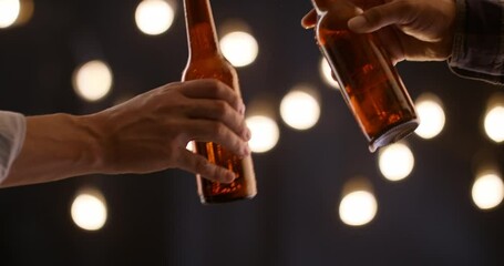 Closeup of male hands clinking beer bottles in festive atmosphere with warm bokeh lights celebration of friendship casual evening moment symbolic gesture of connection party cheers toast night vibe