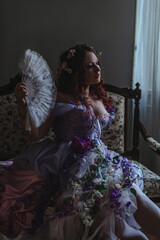 A girl dressed in the style of a Victorian boudoir, in a corset and crinoline of lilac color, in flowers