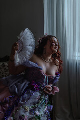 A girl dressed in the style of a Victorian boudoir, in a corset and crinoline of lilac color, in flowers