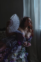 A girl dressed in the style of a Victorian boudoir, in a corset and crinoline of lilac color, in flowers