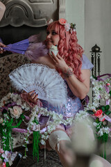 A girl dressed in the style of a Victorian boudoir, in a corset and crinoline of lilac color, in flowers