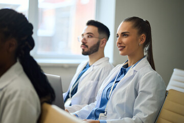 Group of medical students engaged in a classroom lecture, wearing lab coats and taking notes. Bright, professional setting with focused and attentive atmosphere