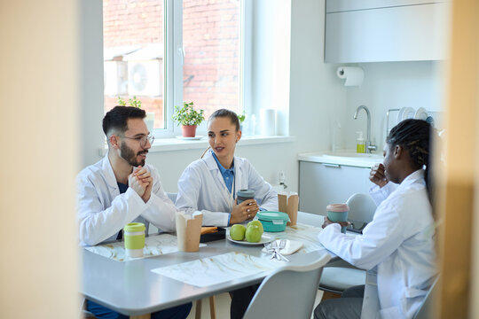 Group of medical professionals enjoying coffee and snacks in a break room while discussing work. Diverse team members in a friendly and relaxed environment, fostering collaboration and camaraderie