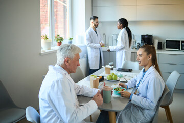 Scientists eating lunch in bright kitchen discussing research findings with colleagues in lab coats