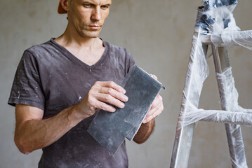 Young non professional man ready for polishing wall with sanding paper. Man using sandpaper mesh to...