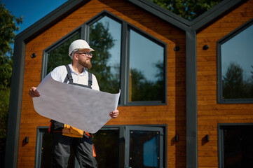 Architect hold plan. Bearded architect wearing hardhat holding project blueprints paper plans...