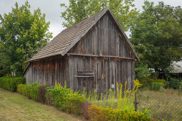 A small, old wooden building with a slanted roof sits in a field