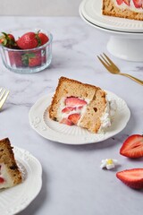 Sliced ​​cake filled with custard and strawberries covered with white icing and decorated with marshmallow flowers on a white plate on a light background. Desserts strawberries.