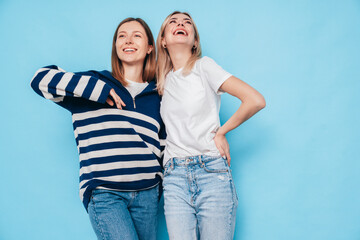 Two young beautiful smiling brunette hipster female in trendy summer clothes. Lovely women posing on blue background in studio. Positive models having fun. Cheerful and happy. isolated