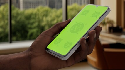 GREEN SCREEN CHROMA KEY A smartphone with a green screen is held in a modern apartment with a city skyline visible through large windows, during the daytime