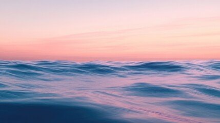 Fototapeta premium A calm ocean with smooth waves under a pastel-colored sky at dusk.