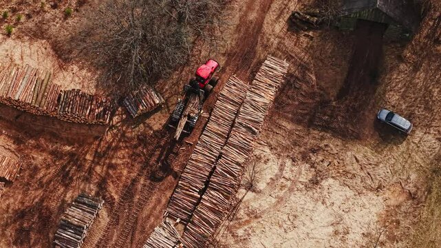 Log forwarder transports timber along dusty road in rural deforested woodland
