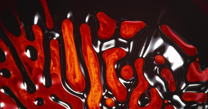 Viscous red streams intertwine with black liquid to form a maze of cellular shapes. The glossy texture and rhythmic flow evoke biological growth and structural deformation in fluid dynamics